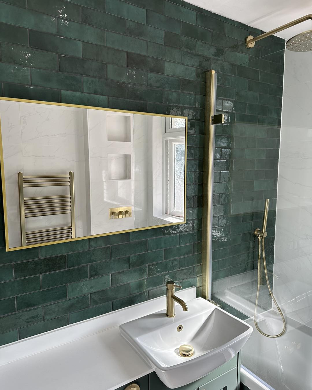 gold mirror hanging in a green tiled bathroom