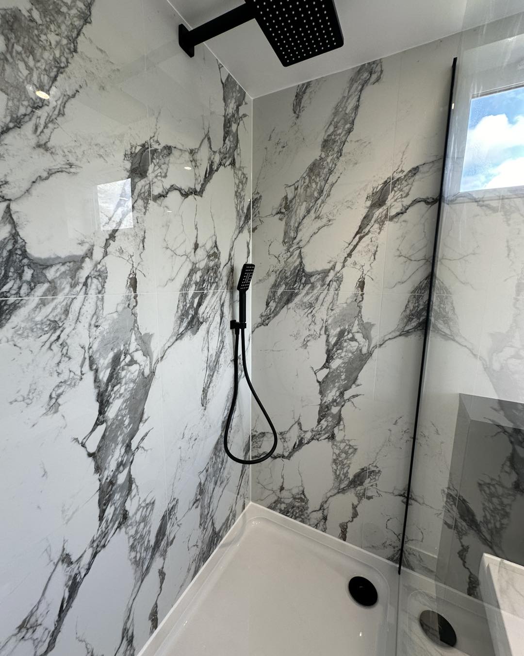 white marble wall tiles and black waterfall shower